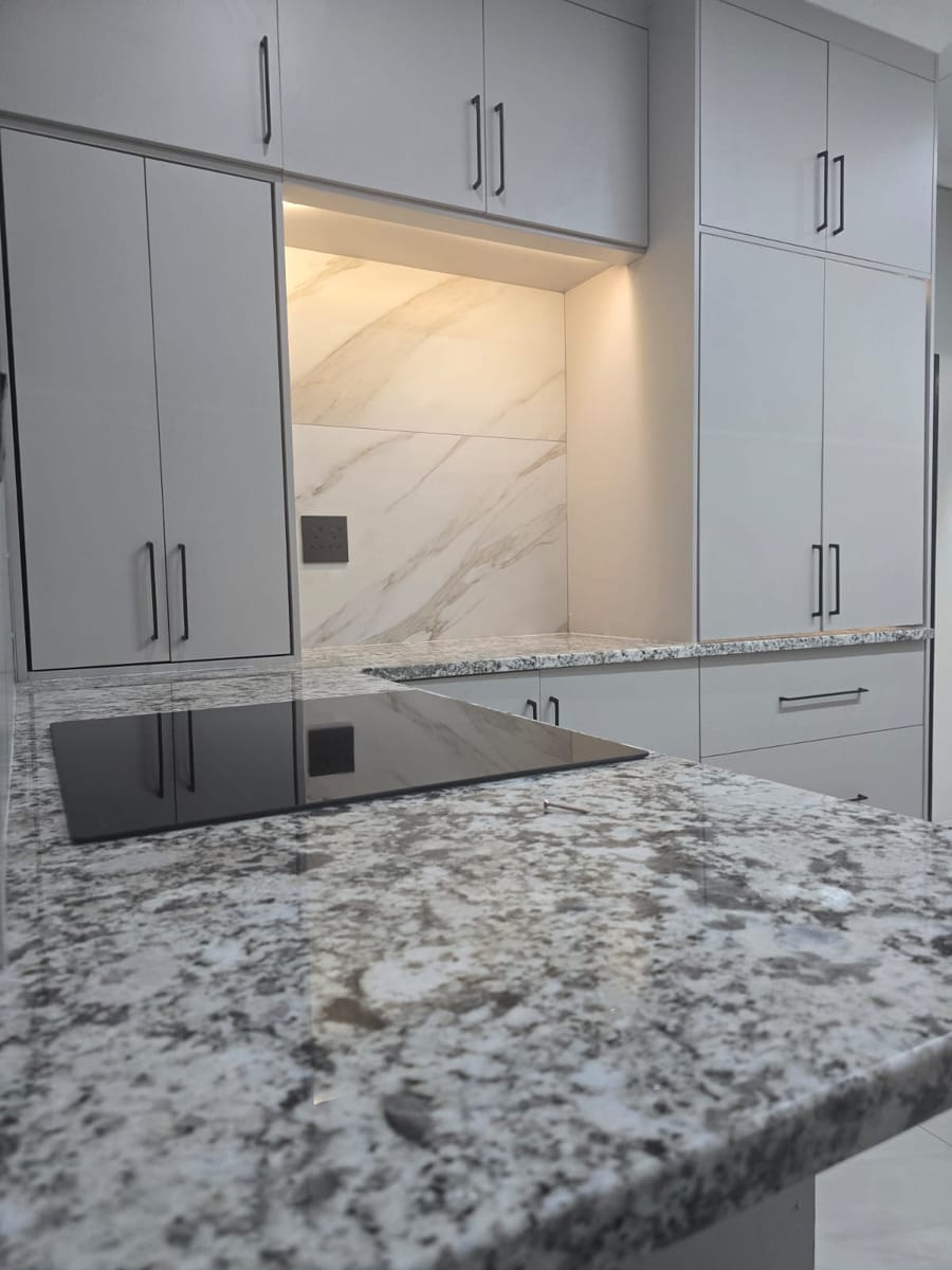 Granite kitchen island with built-in induction hob facing tall white cupboards