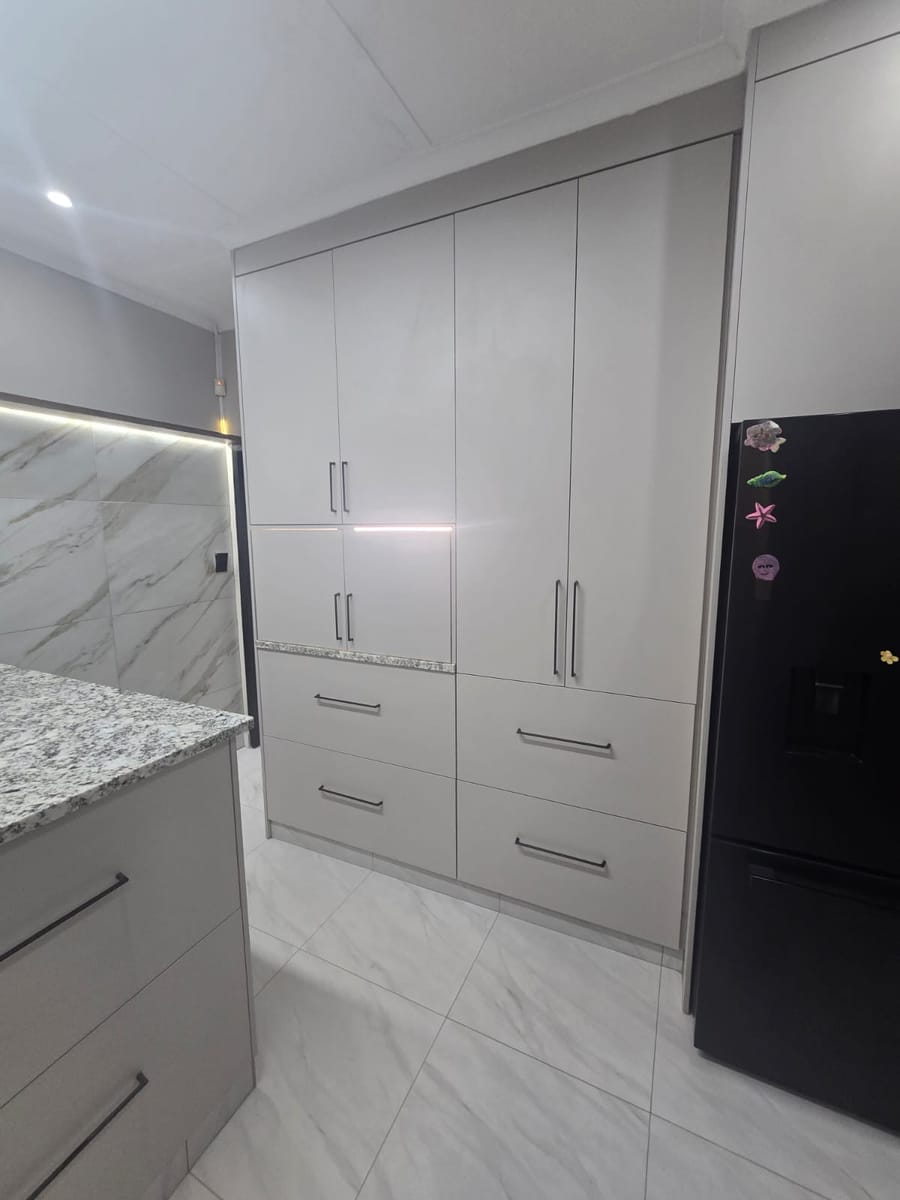 Floor-to-ceiling white kitchen cupboards and drawer stack with black handles